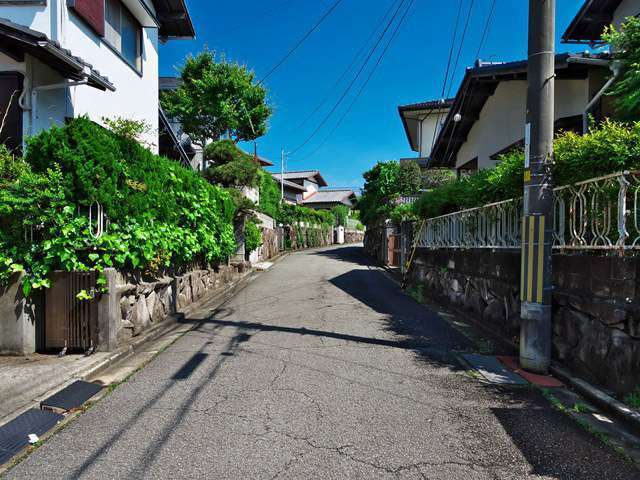 町の北部を南方向から見た景色。緩やかな坂道沿いに生垣や植栽のある一戸建てが並んでいます。
