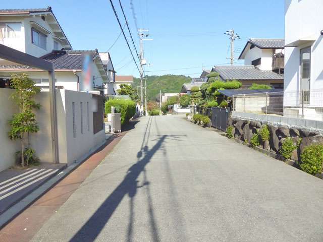 町の中央部を南方向から見た景色。生垣や植栽のある家が多く、奥には山林が広がっています。