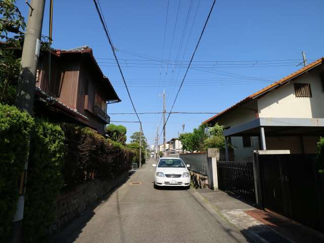 町の東部を西方向から見た景色。幅がやや狭い街路沿いに生垣や植栽のある一戸建てが並んでいます。