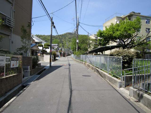 道幅がやや狭い街路沿いに一戸建てや団地が混在しています。奥には箕面の山々が見えます。