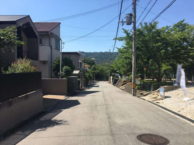 町の西部を南方向から見た景色。生垣や植栽のある家が多く、奥には箕面の山々が見える緑豊かな住環境です。