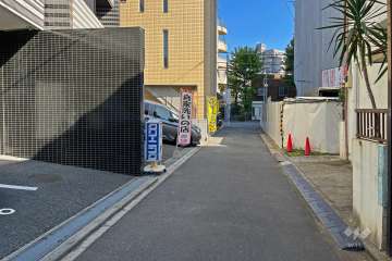敷地の南側前面道路（西側から）。1階部分にクリーニング店があります。
