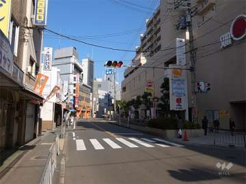 敷地西側の前面道路。周辺は各種店舗が多く立ち並ぶ商業地です。