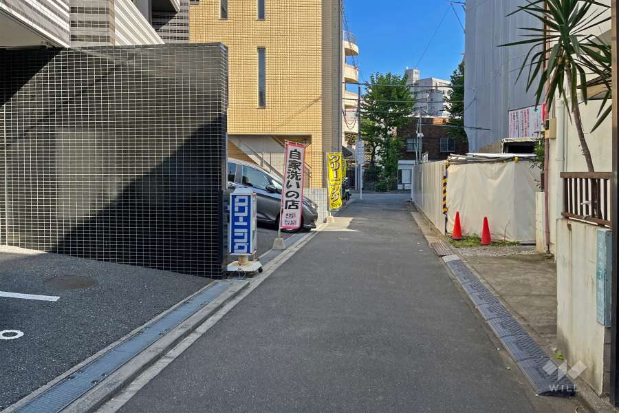 敷地の南側前面道路（西側から）。1階部分にクリーニング店があります。