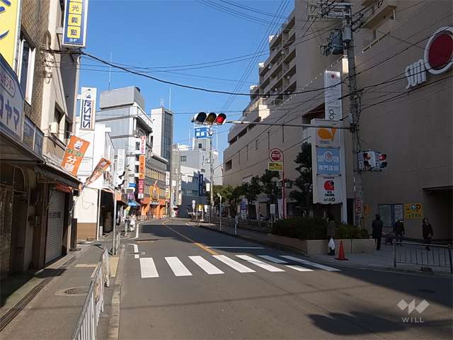 敷地西側の前面道路。周辺は各種店舗が多く立ち並ぶ商業地です。