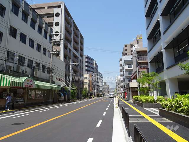 敷地東側の前面道路。商業地域内にあり、マンションの他に、店舗やテナントビルが混在します。